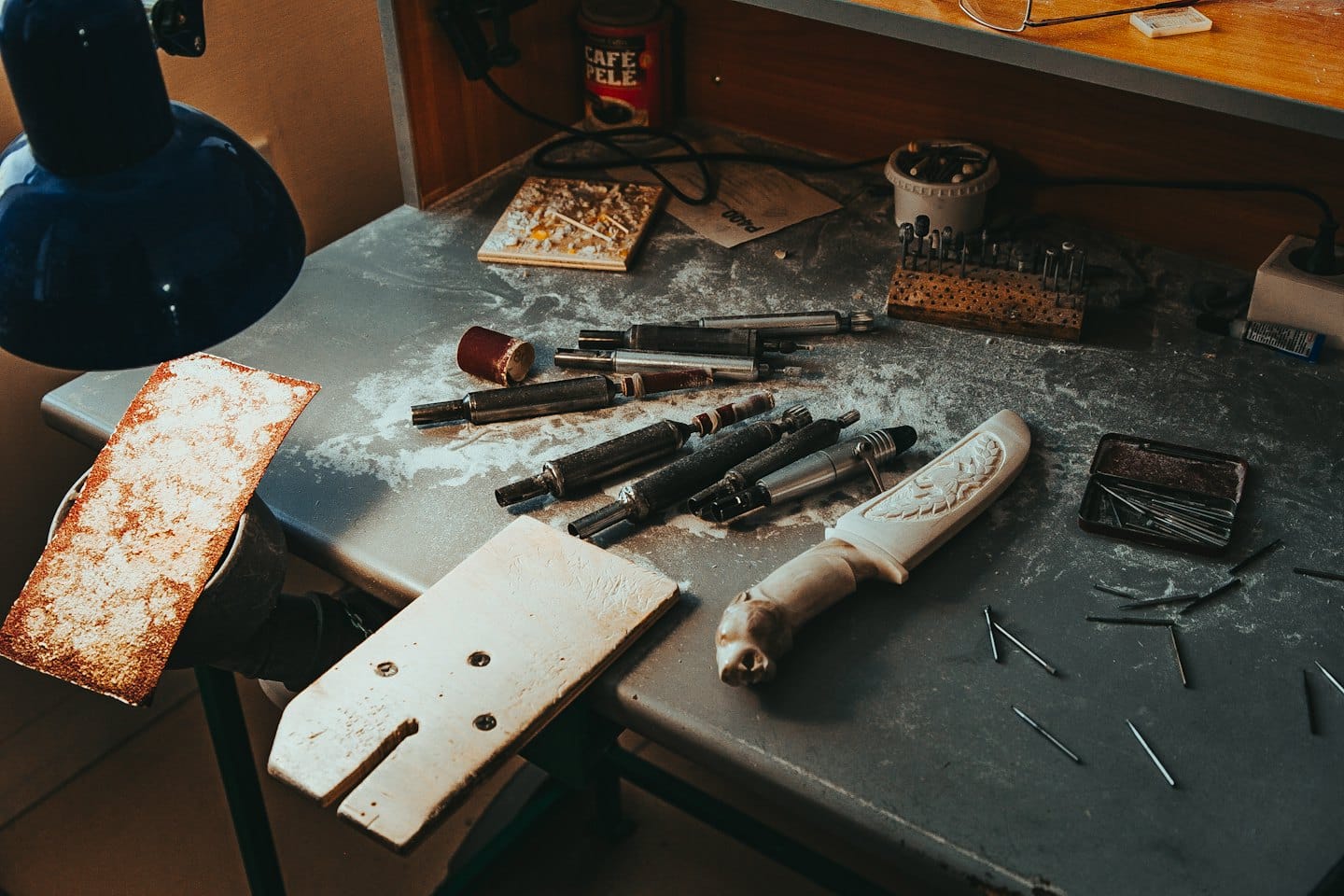 Attrezzi da artigianato e un manico intagliato con cura sono su un banco da lavoro.