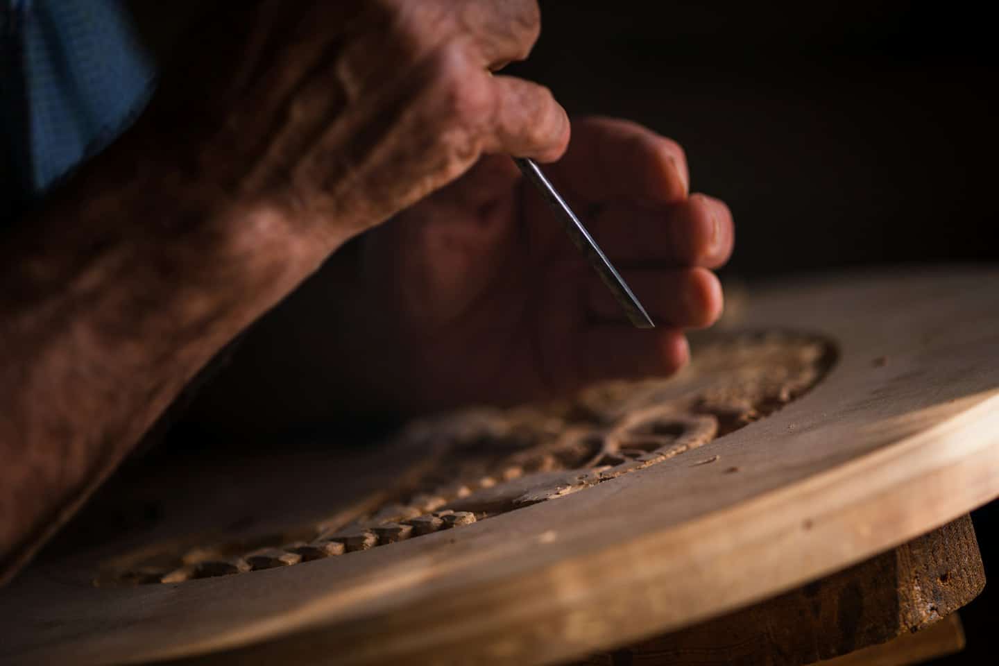 Mani che intagliano motivi intricati nel legno con uno scalpello.